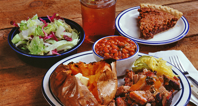 BBQ, baked potato, and baked beans on a plate, a salad on a side plate, a slice of pie on a side plate, and a mason jar of tea